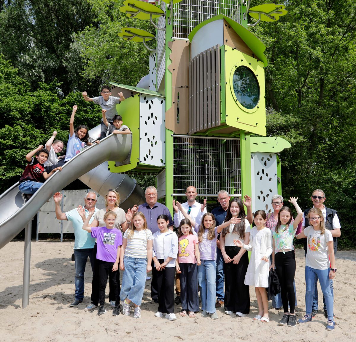 Kinder und Erwachsene posieren gemeinsam vor dem Kanopé-Turm von Proludic, während andere die Edelstahlrutsche nutzen