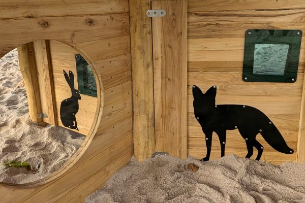 Detailaufnahme einer Holzwand im Spielgerät mit schwarzen Tier-Silhouetten von Hase und Fuchs.