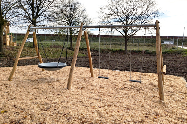 Doppelschaukel aus Holz mit Nestschaukel und zwei klassischen Schaukelsitzen auf einer Fläche mit Holzhackschnitzeln.