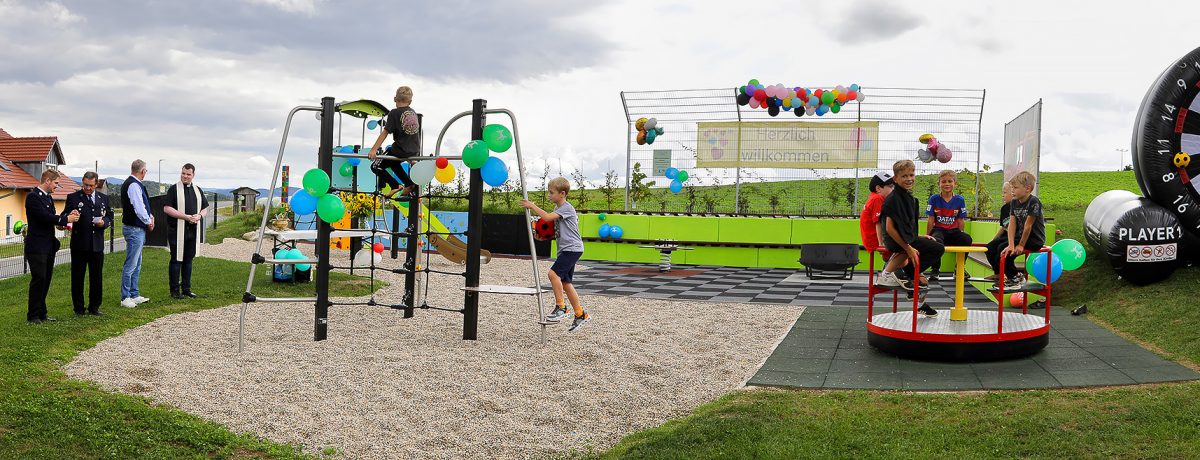 Spielplatz-Eröffnung in Höhhof mit Kindern am Karussell und Klettergerüst sowie Segnung durch Pfarrer und Feuerwehr