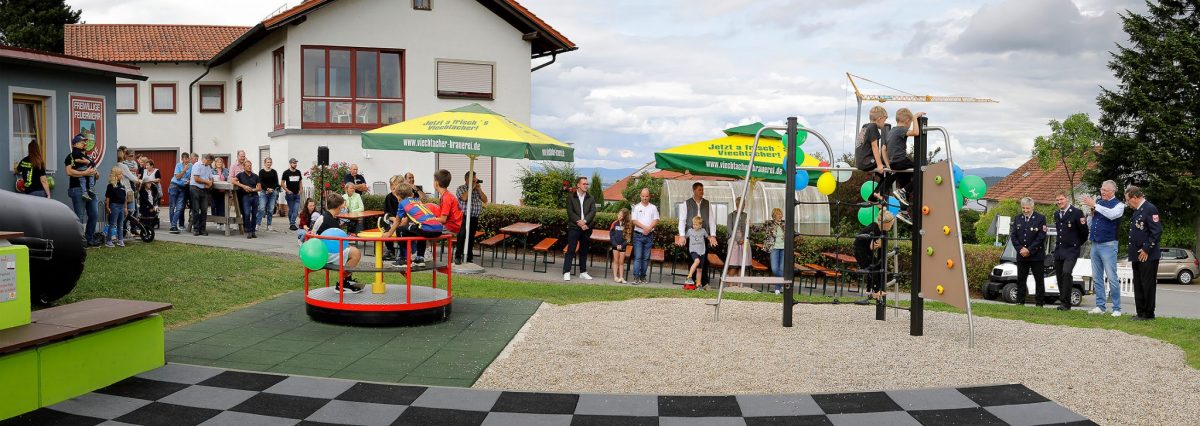 Blick auf die Spielplatz-Eröffnung in Höhhof mit Karussell, Kletteranlage, Familien und Feuerwehr
