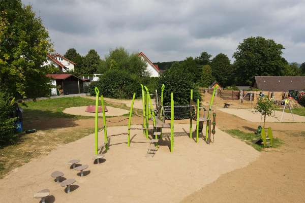 Spielplatz mit Kletter- und Balancieranlage aus grünen Pfosten, Netzen, Seilen, Kletterelementen und Trittplatten in einer großen Sandfläche, im Hintergrund weitere Spielgeräte.