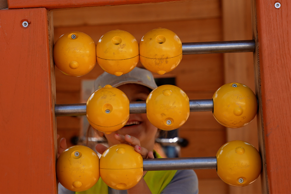Kind spielt fröhlich an einer gelben drehbaren Rechen- oder Abakus-Spieltafel aus robustem Holz und Metall auf einem Spielplatz.