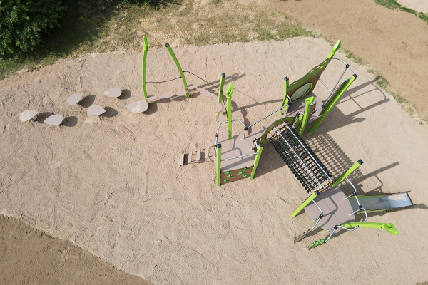 Spielplatzanlage aus der Vogelperspektive, bestehend aus Kletter- und Balancierelementen, Netzbrücke, Leitern, Rutsche und Trittplatten auf einer großen Sandfläche.