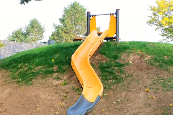 Orangene Hangrutsche auf einem begrünten Hügel des Spielplatzes in Annerod, ideal zum Rutschen und Toben für Kinder.