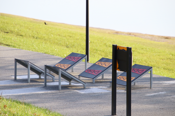 Ninija-Hinderniselemente mit schrägen Rampen auf einem Outdoor-Parcours, angelegt auf Asphaltfläche in naturnaher Umgebung.