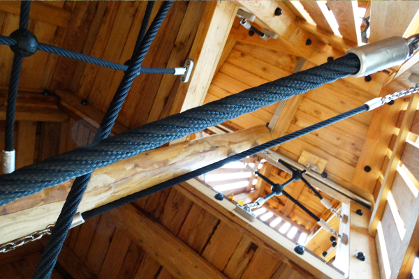 Detailaufnahme im Inneren eines hölzernen Spielturms mit dicken Kletterseilen und Holzkonstruktion.