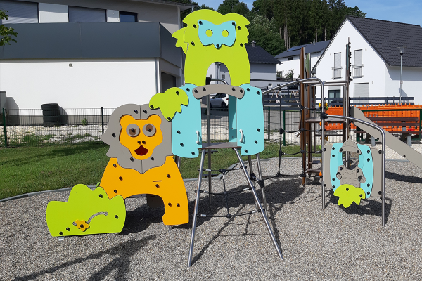 Spielplatz mit farbenfrohen Kletter- und Rutschelementen in Tieroptik, auf Kiesfläche, umgeben von moderner Wohnbebauung.