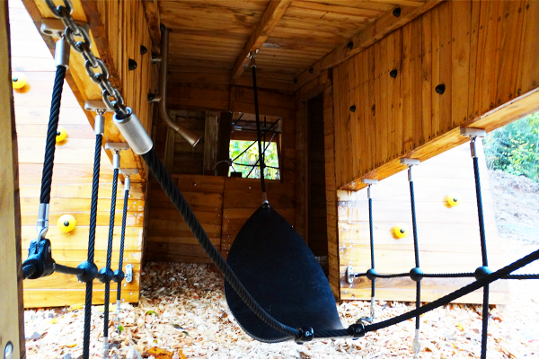 Innenansicht des Hirsch-Spielgeräts mit Kletterseilen, Balanciernetz und Sitzschale, umgeben von Holzstruktur.