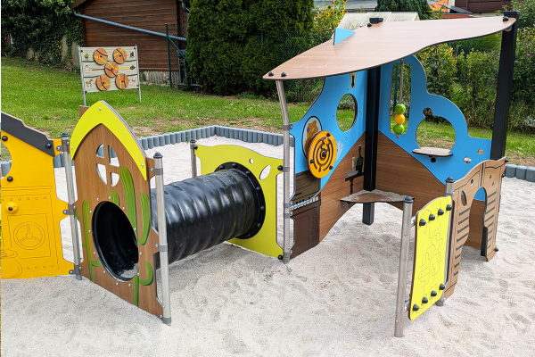 Detailansicht eines Spielmoduls mit Kriechröhre, interaktiven Spielelementen, Motoriktafel und hölzernem Rollenspielbereich im Western-Stil, auf hellem Sandspielboden.
