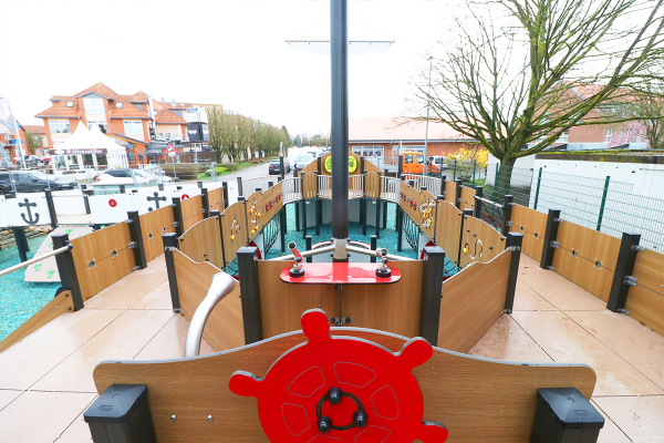 Blick vom Spielschiff auf den barrierefreien Innenraum des inklusiven Spielplatzes in Weyhe mit Spielwand-Elementen und Steuerstand.