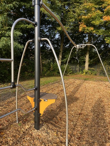 Seilbahn „Skyrail“ mit geschwungenen Edelstahlstützen und einer hohen Startplattform; eine Griffrolle hängt am oberen Seil, darunter Holzhackschnitzelboden und herbstliche Bäume im Hintergrund.