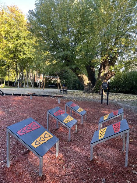 Fünfsprung-Element mit fünf unterschiedlich geneigten Sprungflächen auf Holzhackschnitzel-Belag im Eichpark Sottrum, im Hintergrund Bäume und weitere Spielgeräte.