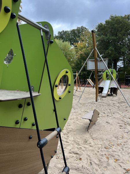 Detailaufnahme des grünen Spielschiffs im Eichpark Sottrum mit Blick auf Kletterelemente und Rutsche, im Hintergrund weitere Spielgeräte auf Sandfläche.