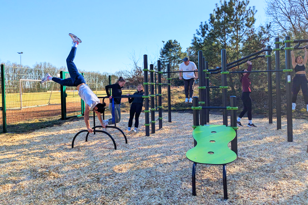 Mehrere Personen trainieren an einer Calisthenics-Anlage im Freien, ein junger Mann macht einen Handstand auf Parallelstangen.