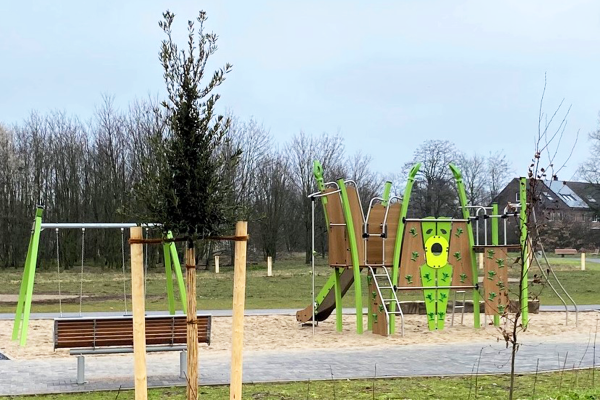Kletter- und Spielanlage mit Rutsche und Schaukeln auf barrierefreier Sandfläche im Park Grüne Mitte Bocholt, mit Sitzbank und junger Baumbepflanzung.
