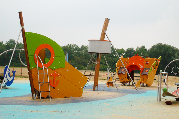 Detailansicht des Piratenspielplatzes mit zwei farbenfrohen Spielschiffen, Kletterleitern und maritimen Spielelementen auf Sandfläche