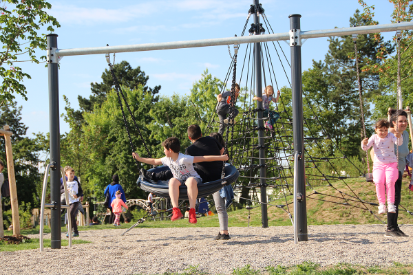 Kinder schaukeln und klettern im Generationenpark Philippsburg bei sonnigem Wetter – begleitet von Erwachsenen und eingebettet in viel Grün.