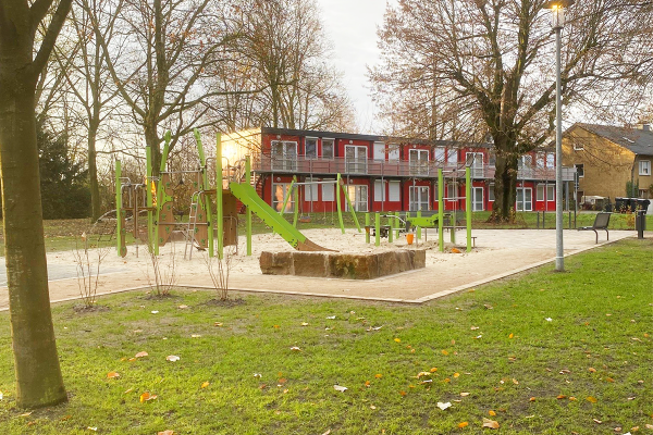 Spielplatz mit Multispielanlage, Schaukel und Sandbereich im Stutenteichpark Waltrop, vor rotem Gebäude im Hintergrund