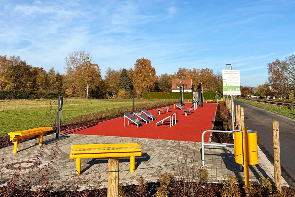 Ninja-Parcours in Menden mit Fitness- und Balanceelementen auf rotem Kunststoffbelag, ergänzt durch Sitzgelegenheiten im öffentlichen Grünraum