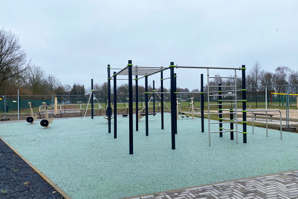 Outdoor-Fitnessbereich mit Street-Workout-Anlage, Klimmzugstangen und Fitnessgeräten auf trittdämpfendem Bodenbelag im Park Grüne Mitte Bocholt.