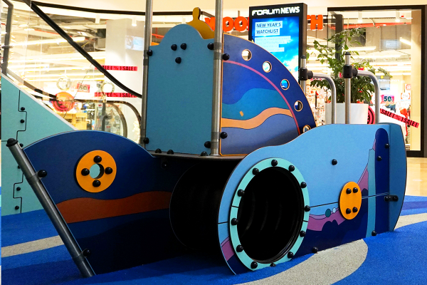 Detailansicht eines maritim gestalteten Spielschiffs für Kleinkinder im Indoor-Spielbereich eines Einkaufszentrums, mit Kletter- und Kriechtunnel sowie farbenfrohen Gestaltungselementen.