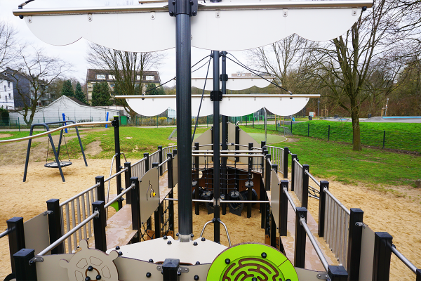 Innenansicht eines großen Spielschiffs mit Steuerrad, Spielboard, Kletternetzen und Geländern auf einem Sandspielplatz