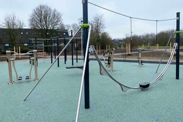 Aeroskate-Trainingsgerät im Vordergrund eines barrierefreien Outdoor-Fitnessbereichs mit weiteren Sportgeräten und Street-Workout-Anlage in der Grünen Mitte Bocholt.