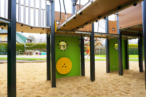 Unterer Bereich eines großen Spielgeräts mit grün-gelber Spieltafel in Form eines Drehzahlzählers, aufgestellt auf einem Fallschutzbelag aus Holzschnitzeln.