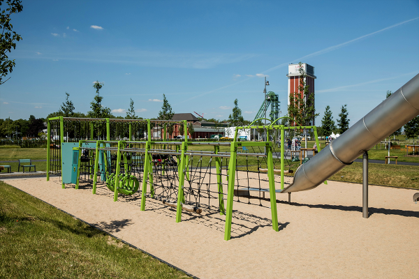 Grün gestalteter Spielparcours mit Netzen, Balancierseilen, Hangelstrecken und Kletterelementen auf einer Sandfläche. Im Hintergrund ist ein Förderturm mit der Aufschrift „LAGA 2020“ zu sehen.