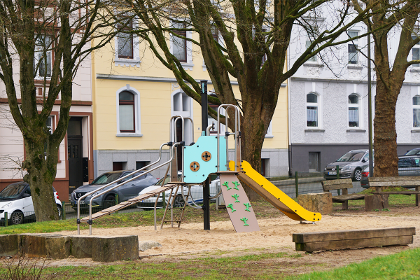 Kompakte Spielkombination mit Rutsche, Kletterwand und Spielpanelen auf einem innerstädtischen Spielplatz mit Sandfläche