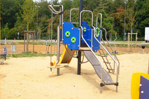Nahaufnahme eines blauen Spielturms mit Rutsche, Kletterrampe, Schaukel- und Balancierelementen auf einem Spielplatz mit Sandboden