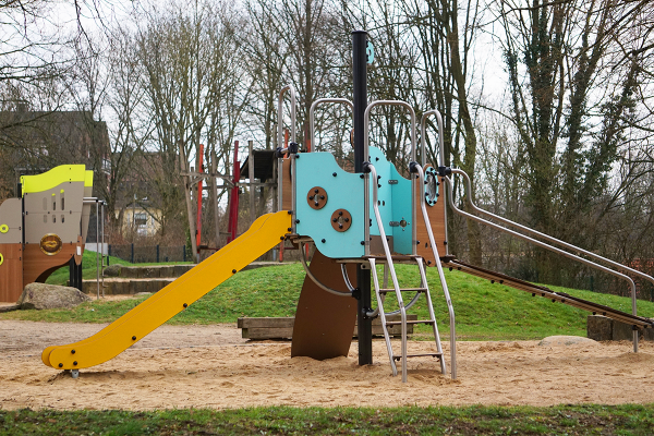 Spielkombination mit bunter Rutsche, Kletterzugängen und taktilen Spielelementen auf Sandfläche im öffentlichen Park
