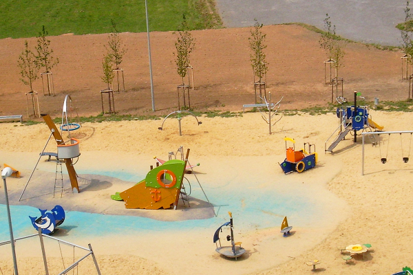 Vogelperspektive auf den Piratenspielplatz mit Spielschiff, Kletterturm, Schaukeln, Karussell und Sandflächen in maritimer Gestaltung