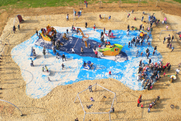 Luftaufnahme des gut besuchten Piratenspielplatzes mit zahlreichen Kindern und Erwachsenen auf blauer Bodenfläche in maritimer Gestaltung