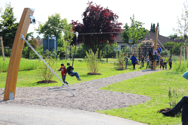 Kinder fahren mit einer Seilbahn über einen Spielbereich im Generationenpark Philippsburg, begleitet von wartenden Kindern im Hintergrund.