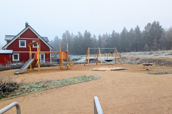 Naturnaher Spielplatz in Buchholz-Sprötze mit Kombinationsspielanlage aus Robinienholz, Rutsche, Schaukel mit Nestschaukel, Sandspielbereich und Federwippe.