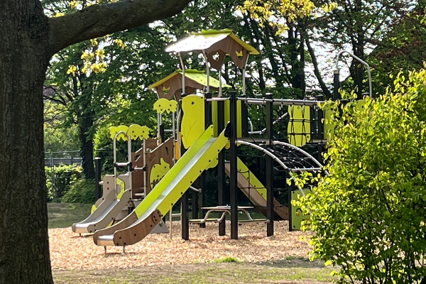 Multiplay-Spielplatzgerät mit zwei Rutschen, Kletter- und Hangelbrücke, eingebettet in eine grüne Parklandschaft mit natürlichem Fallschutz.