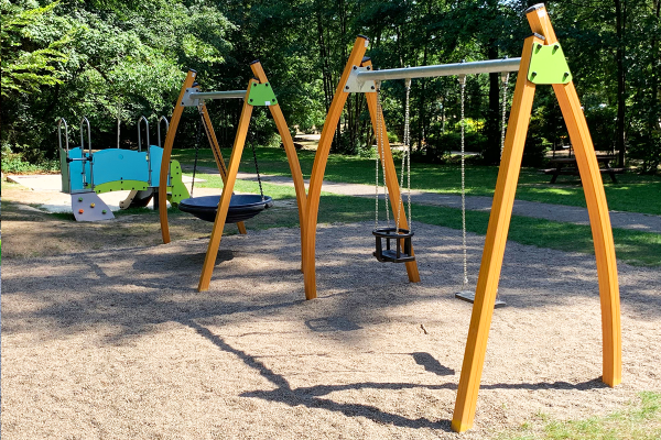 Kanopé-Schaukelanlage aus Holz mit Nest- und Kleinkindschaukel, im Hintergrund Diabolo-Spielanlage auf dem Spielplatz Westertal in Bad Sachsa