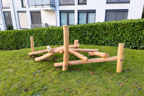 Mikado L Balancierstämme aus Naturholz auf Rasenfläche in einem Wohnquartier.