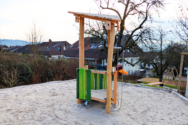 Naturholz-Spielhaus mit Sandaufzug und überdachtem Podest in einem Sandspielbereich auf einem Quartiersspielplatz.
