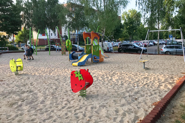 Sandspielplatz in Rostock mit Federwippgeräten im Vordergrund, Rutsche, Kletteranlage und Schaukel im Hintergrund