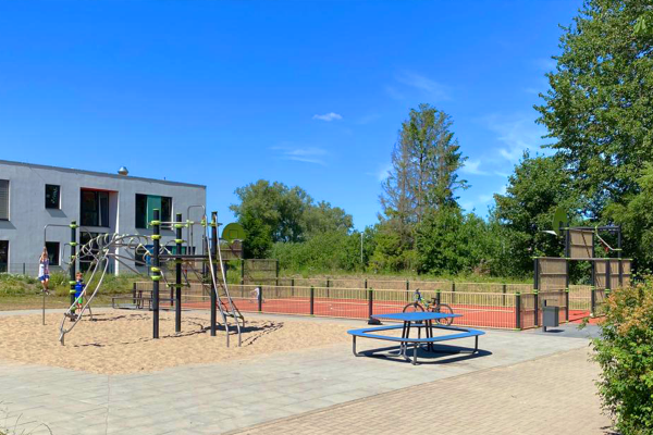 Schulhof mit IXO Kletteranlage im Sandbereich und angrenzender Multisportanlage mit rotem Spielfeld an der Grundschule Kritzmow