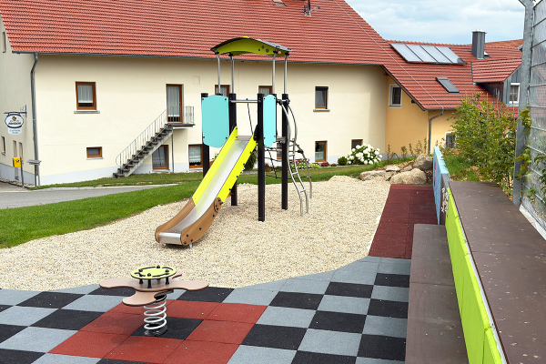 Proludic Spielturm mit Rutsche und Federwippe auf Fallschutzbelag auf dem Spielplatz Höhhof im ländlichen Wohnumfeld.
