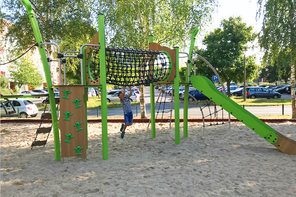 Kind spielt auf einer Kanopé-Kletteranlage mit Netzbrücke und Rutsche auf einem Sandspielplatz in Rostock