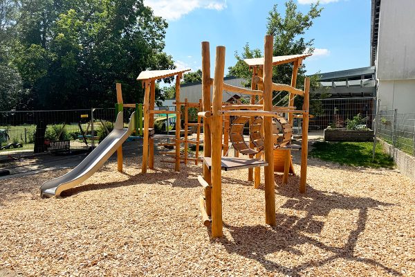 Individuelle Holzspielanlage mit Rutsche, Kletterelementen, Spieltunnel und erhöhten Plattformen im Kinderhaus Montessori Sonnenhaus in Maxhütte-Haidhof.