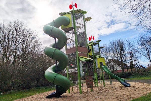 Hoher Kanopé-Spielturm auf dem Spielplatz Am Steinkamp in Burg auf Fehmarn mit spiralförmiger Röhrenrutsche, Kletterelementen und Sandspielfläche.