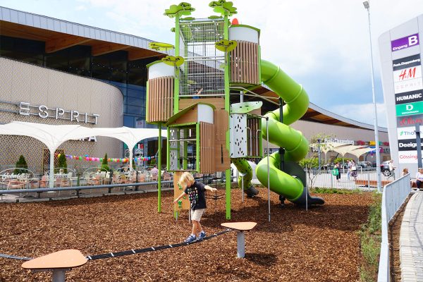 Kanopé-Spielturm von Proludic vor dem G3 Shopping Resort in Gerasdorf bei Wien mit großer Röhrenrutsche, Balancierstrecke und naturnah gestaltetem Spielbereich.
