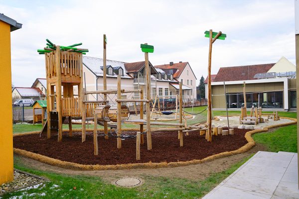 Kombinationsspielanlage aus Naturholz mit Nestturm, Balancierpfad und Kletterelementen auf dem Außengelände der Kita Karlskron.