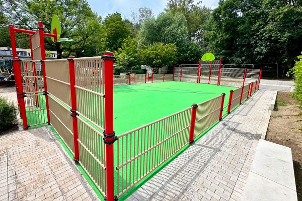 Multisportanlage an der Hirschkampschule in Oberhausen mit Basketballkörben, Ballfangzaun und grünem Spielfeld.